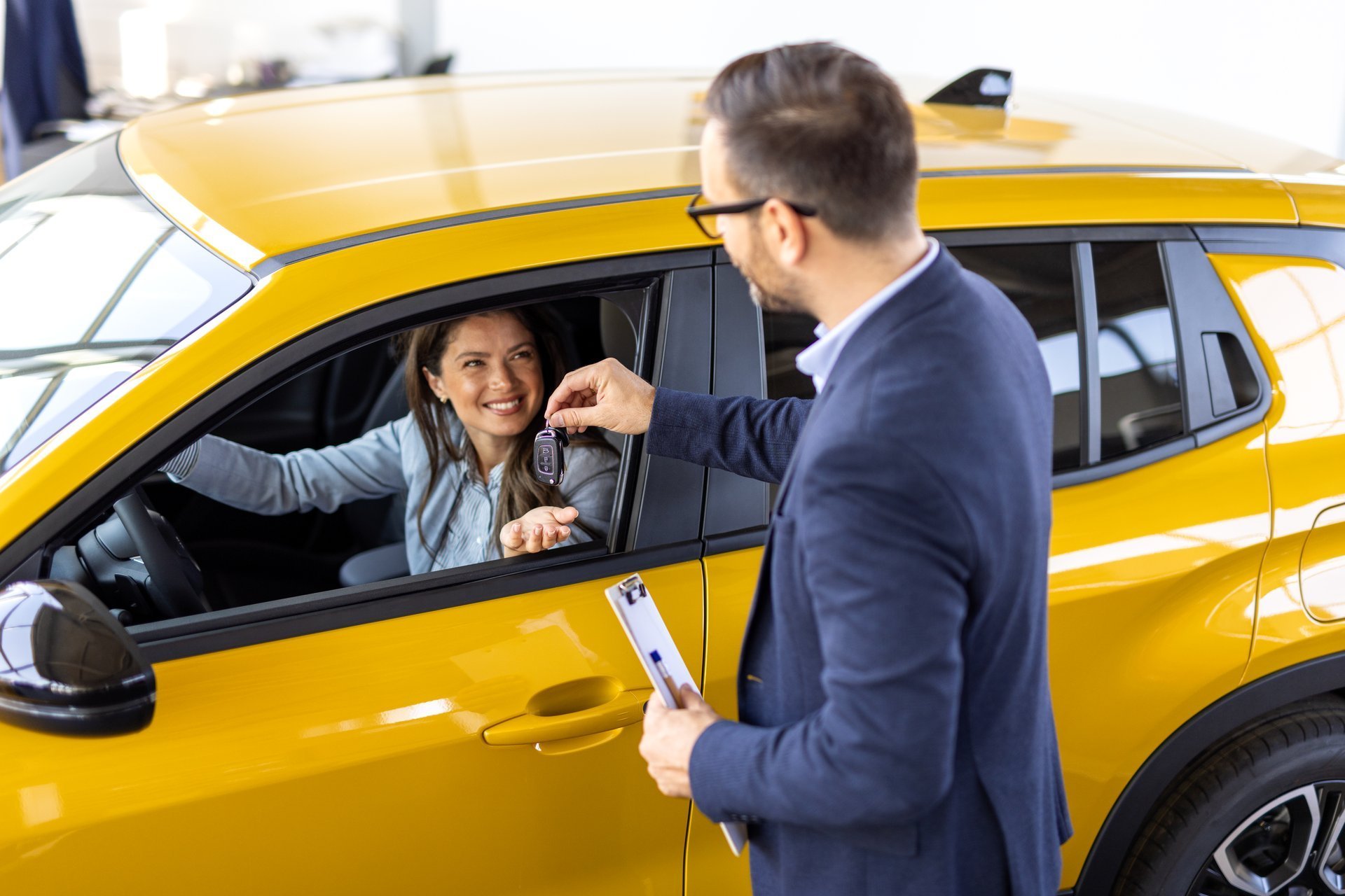 Woman receiving car keys from a rental car employee while sitting in a rental vehicle.