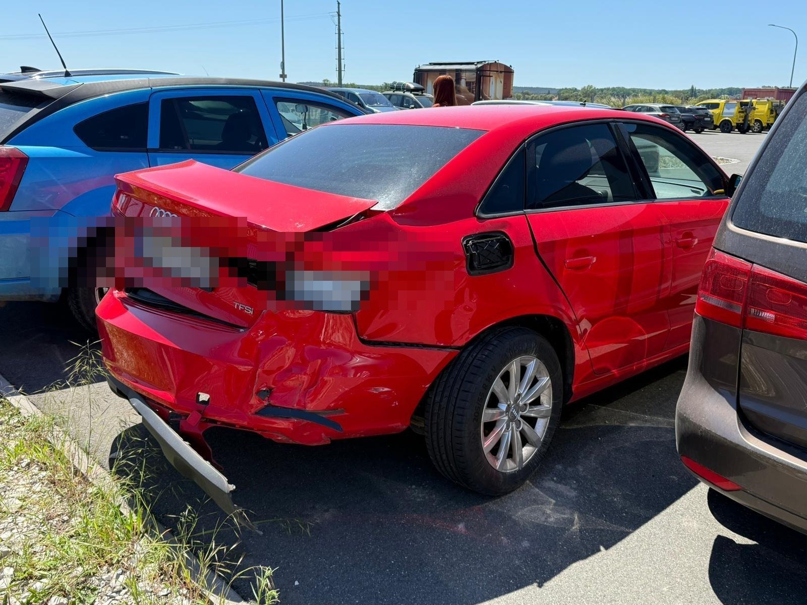 Red damaged car with crumpled rear bumper in salvage yard with other vehicles