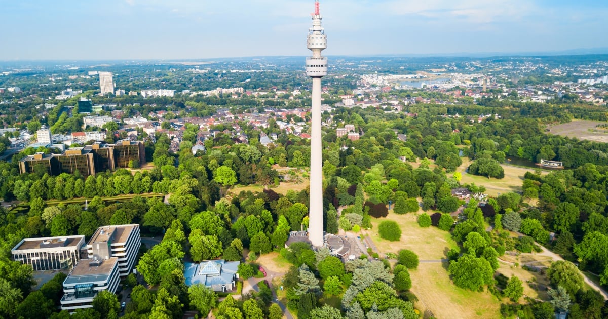 Aerial view of a white telecommunications tower rising above a green suburban landscape with buildings and trees