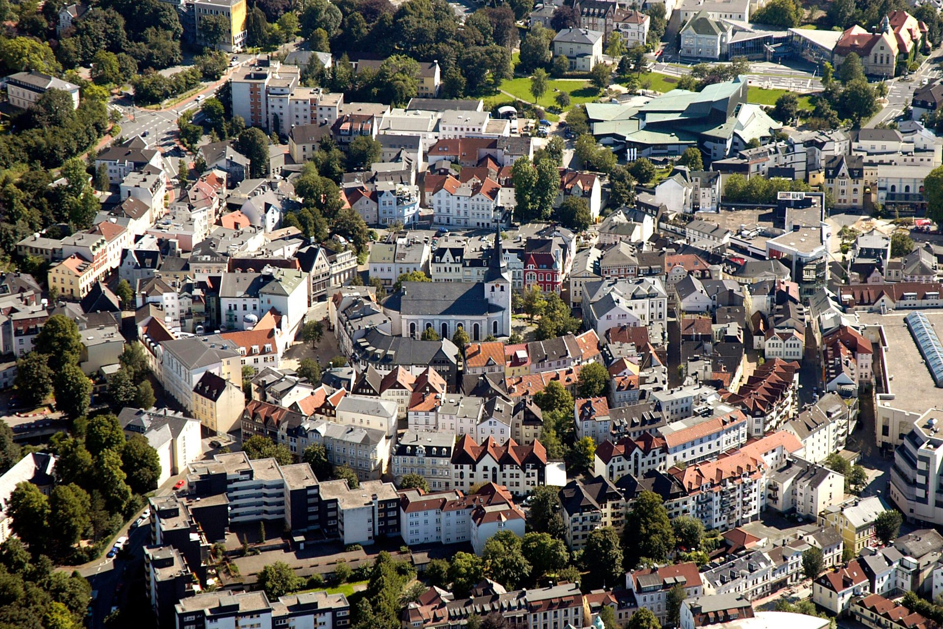 Aerial view of a European town with historic architecture, red-tiled roofs, tree-lined streets, and residential buildings