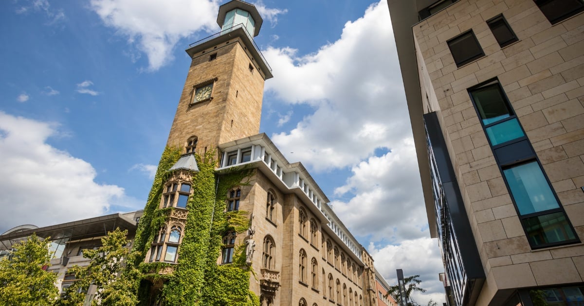 Ivy-covered historic stone building with clock tower under blue sky with white clouds
