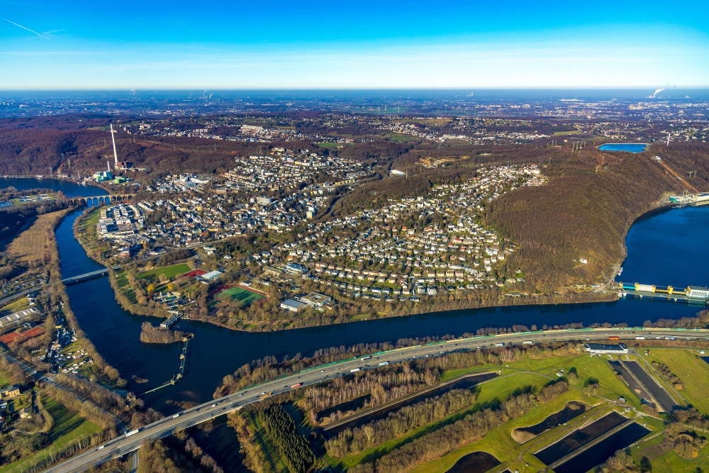 Aerial view of suburban landscape with winding river, residential neighborhoods, and forested areas under clear blue sky