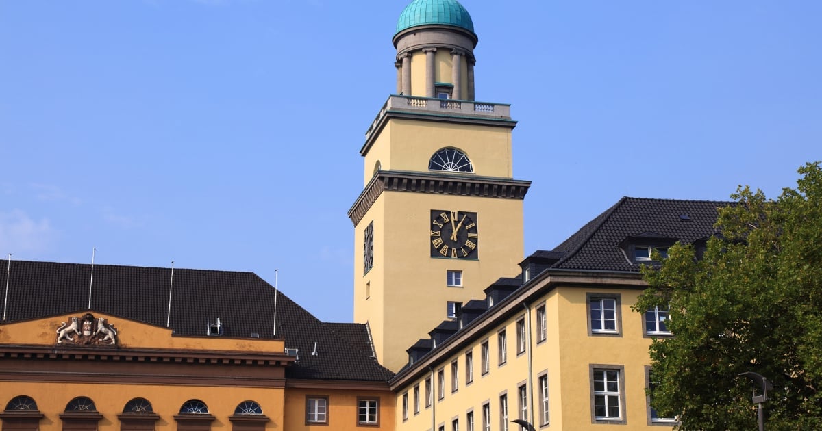 Historic yellow building with tall clock tower featuring green copper roof against blue sky
