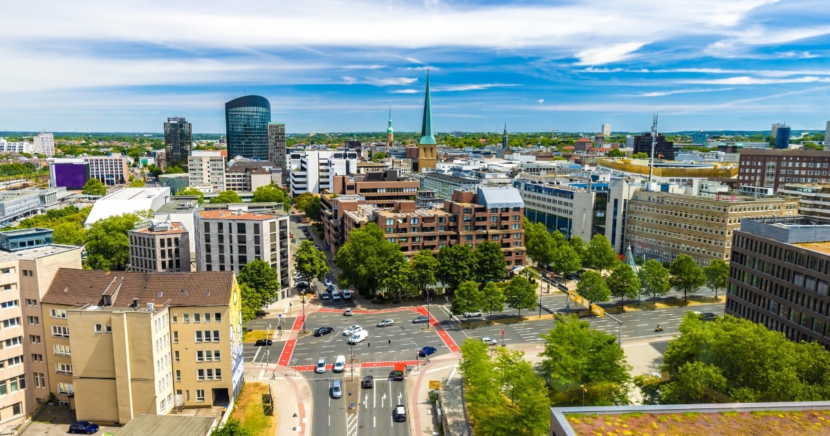 Aerial view of a European city with residential buildings, modern skyscrapers, green parks, and streets under blue sky